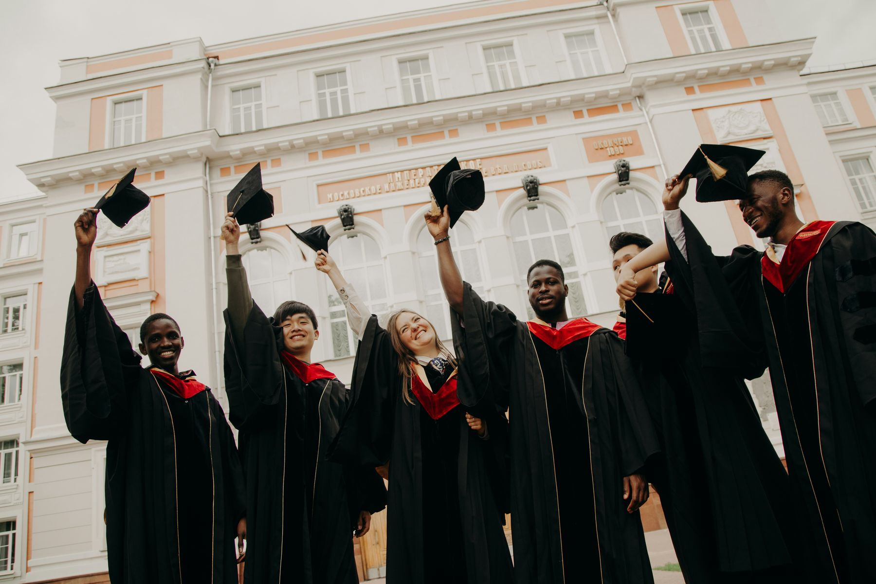 International graduates in gowns raising their caps outside their university