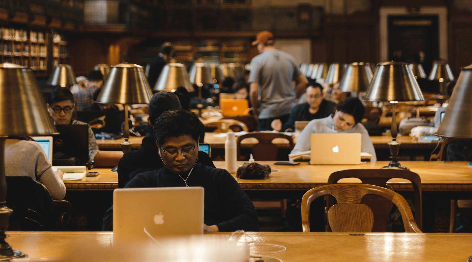 Students working at library desks under brass reading lamps